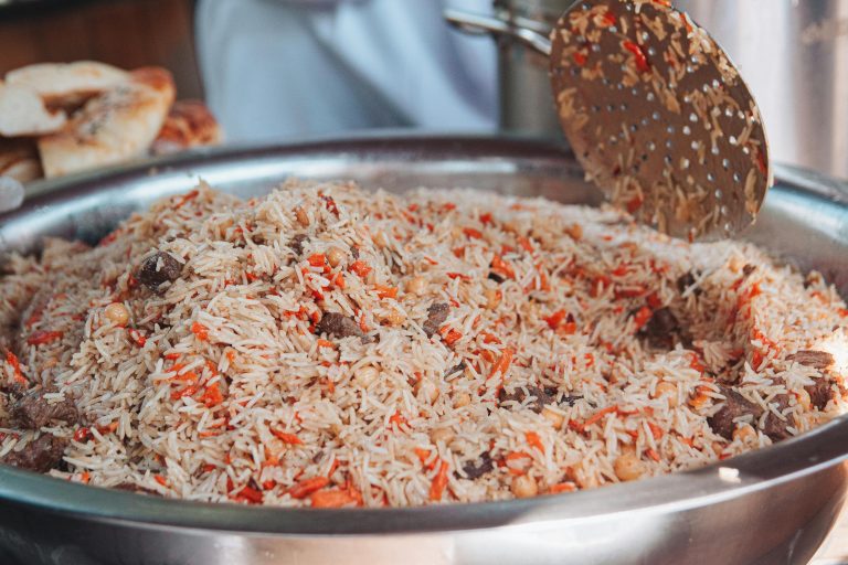 Close-up of freshly prepared plov with meat and carrots in a stainless steel pot, showcasing vibrant colors and textures.