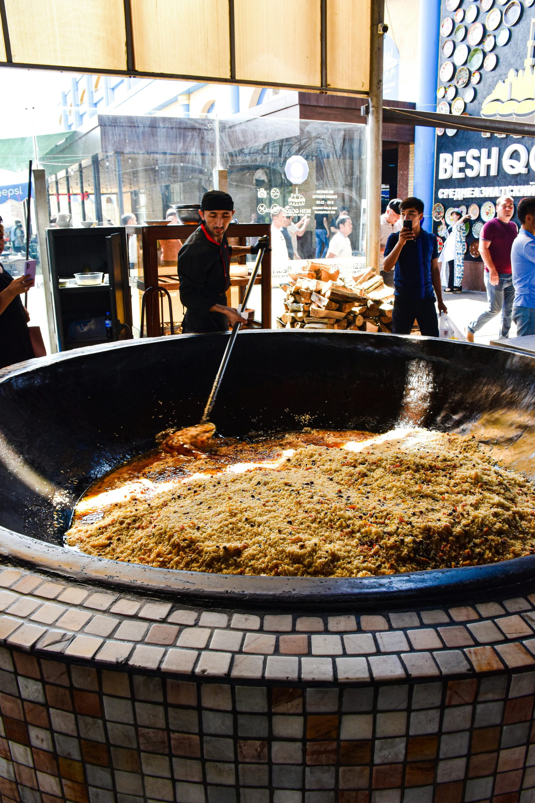 Man cooking large pot of traditional plov outdoors, surrounded by onlookers.